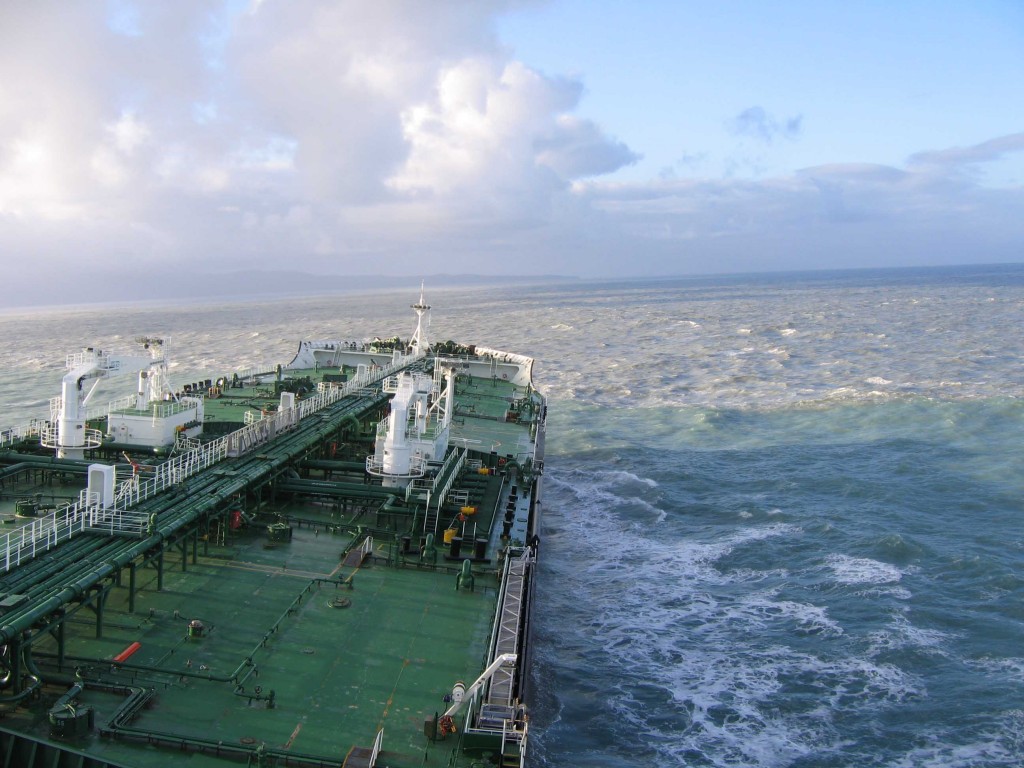 Photo from on board a ship, showing a green bow jutting out into the ocean