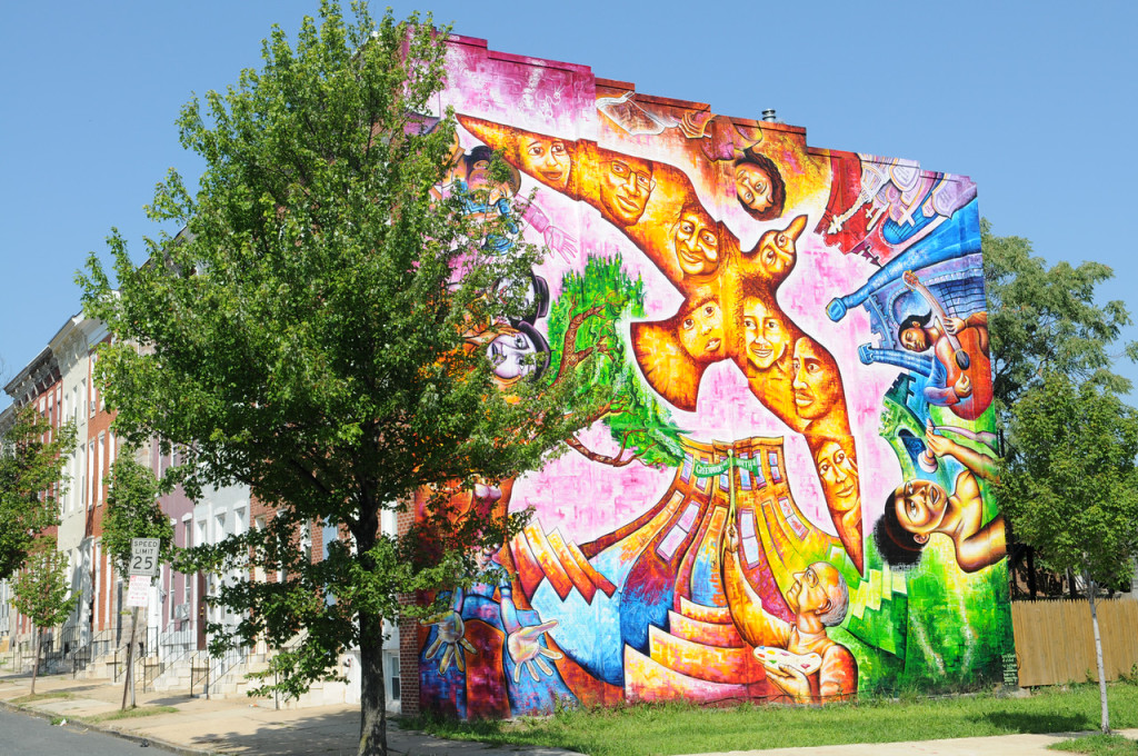 Wall art on a Baltimore building: A golden bird full of faces rises from a tree and a city building.