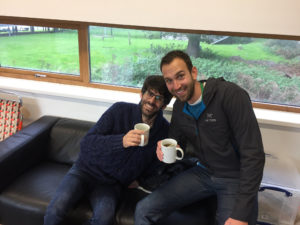 Two men sitting on couch with mugs.