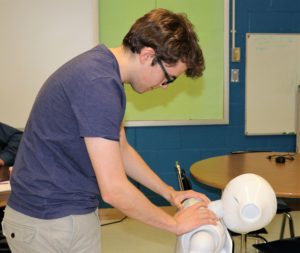 A high school boy examines a white robot