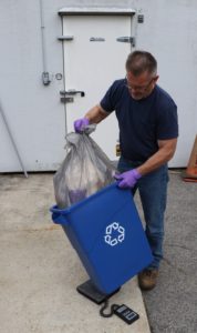 Man pulls plastic bag out of blue recycling bin