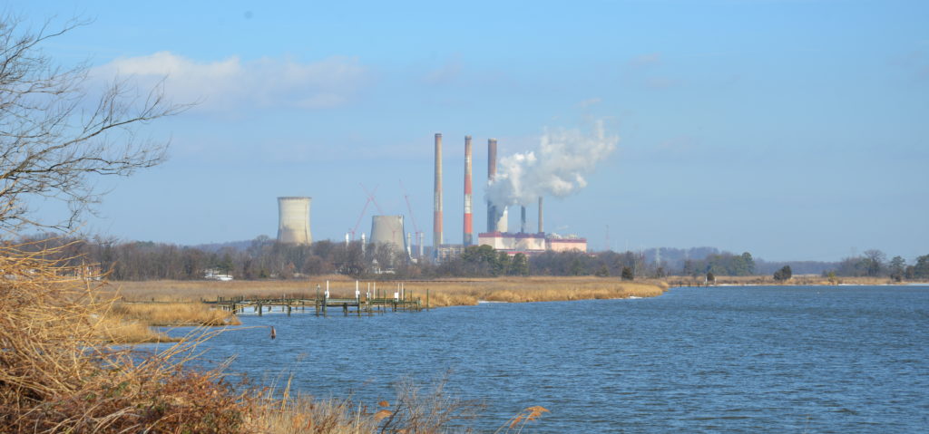 Photo of a river with a power plant in the background, white smokestacks billowing above it.
