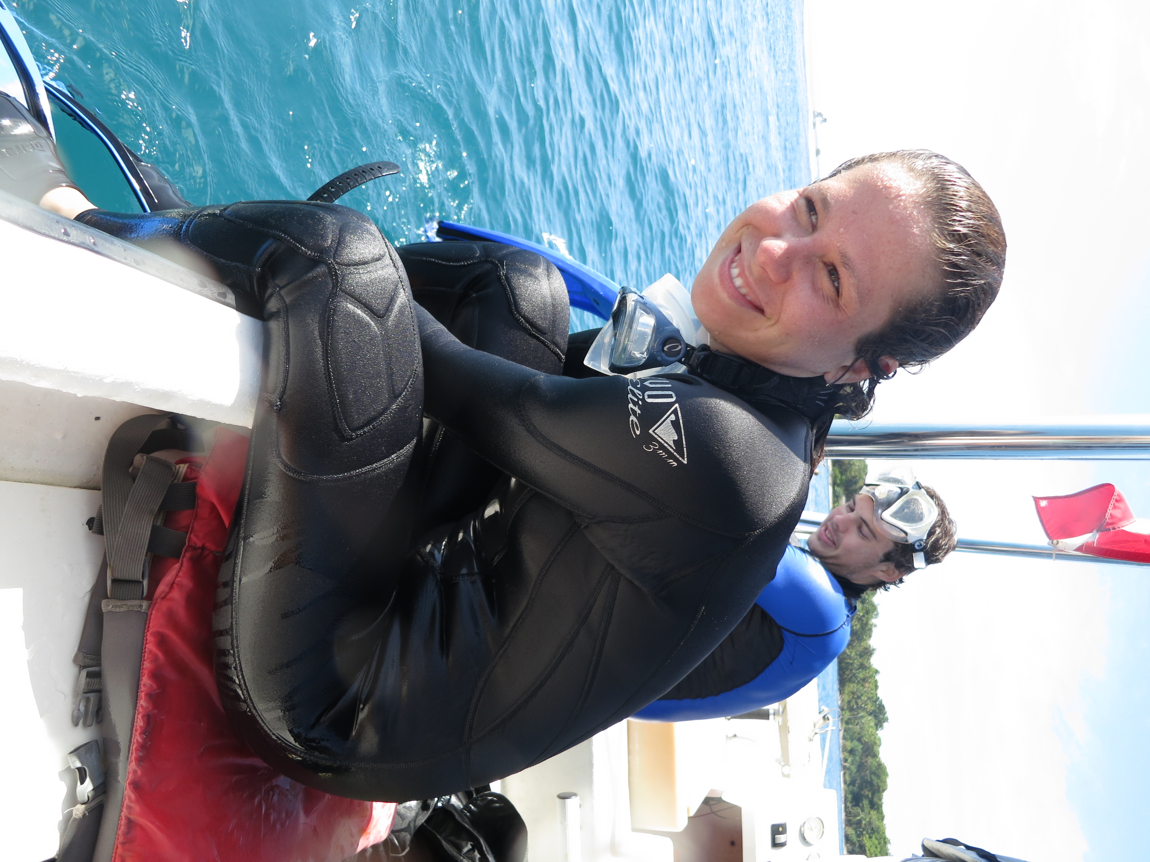 Young woman sitting on boat in black wetsuit