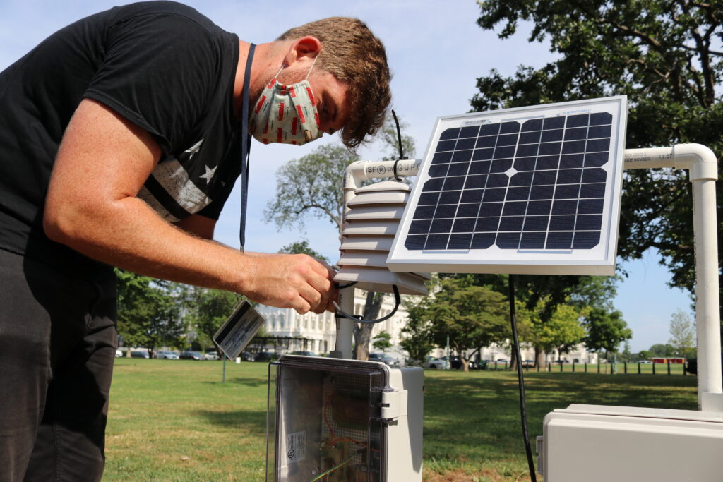 Young man in mask on a green lawn next to solar panel