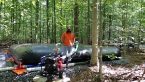Man in forest in front of giant black rubber tank