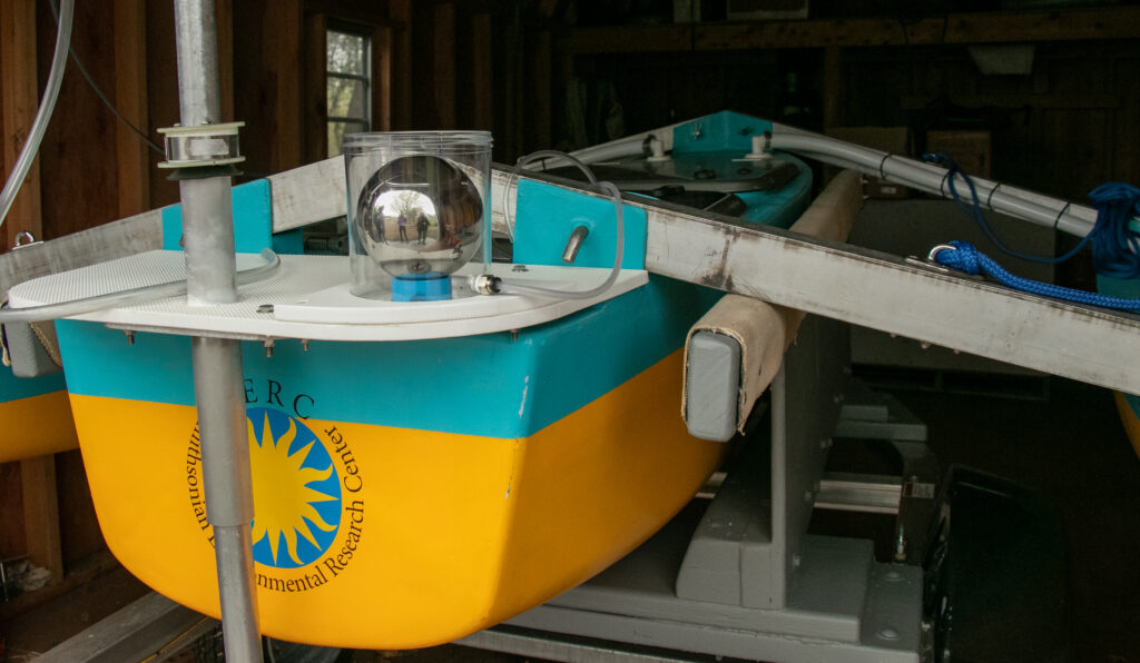 Large silver ball in clear container, on top of blue and yellow research boat