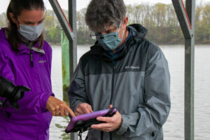 Woman in purple jacket and man in gray jacket look at tablet on a floating dock
