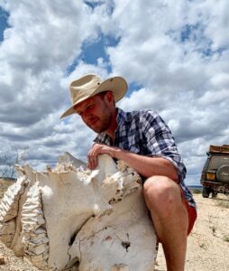 Man in straw hat kneeling beside elephant skull in desert