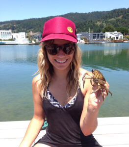 Young woman on dock holds up a green crab