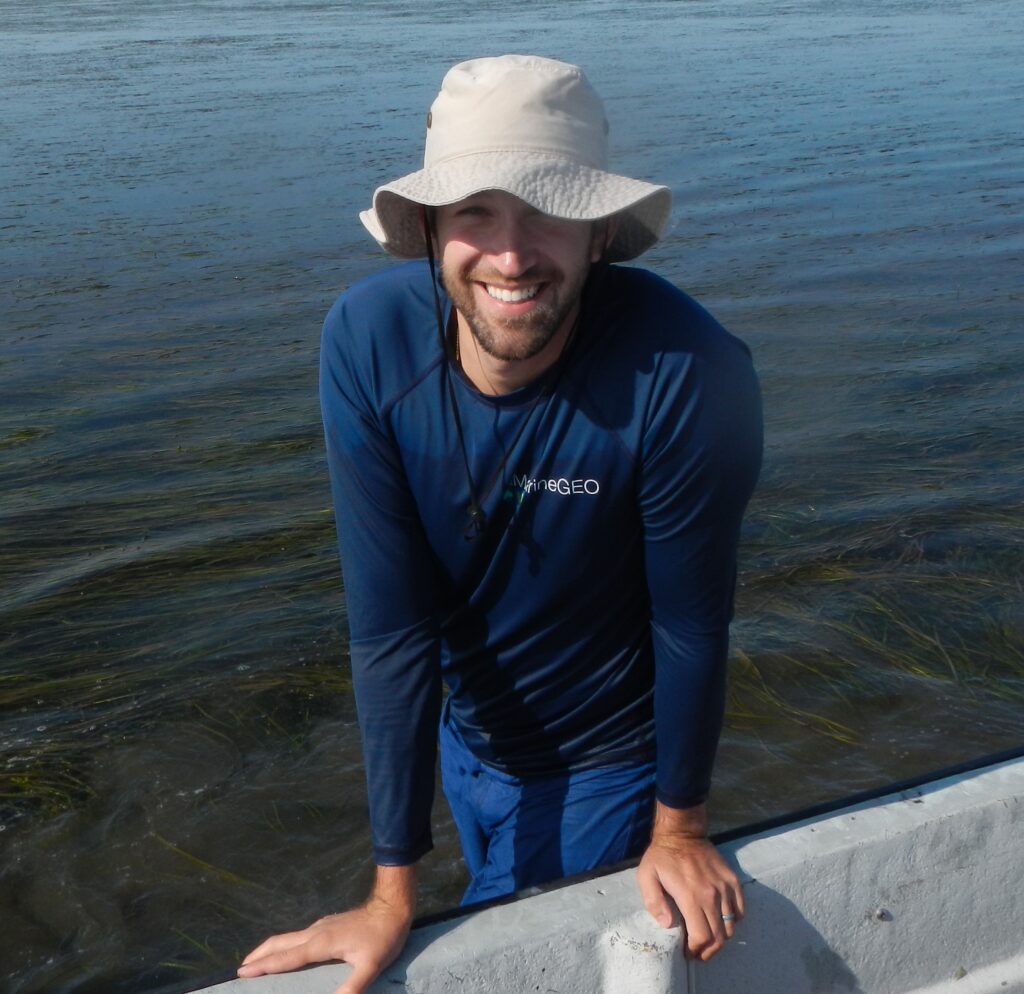 Man wading in water, in navy shirt and floppy khaki hat