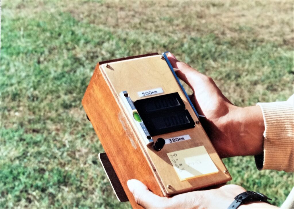 Closeup of a brown wooden box held in two hands. Small black and silver instrumentation rest on top of the box.