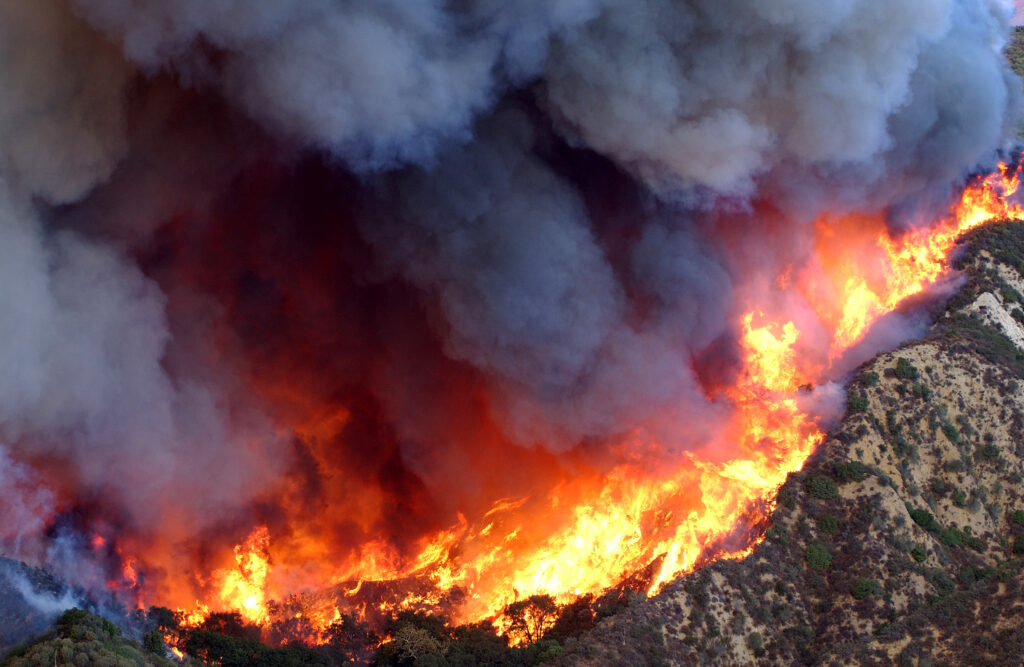 Gray smoke billows from fires on a mountainside, as seen from above.