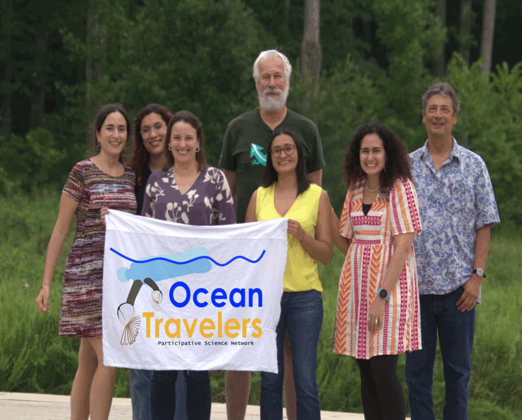 Seven people pose behind a white banner with the words "Ocean Travelers"