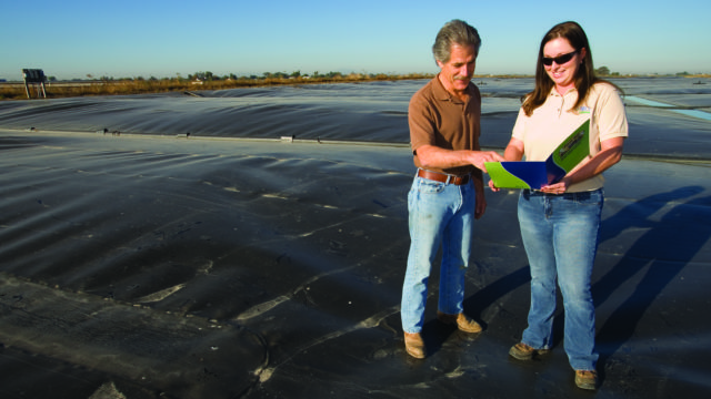 Man and woman stand on methane digester looking at folder.